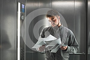 Portrait of a office worker examining the documents in the elevator.Close up photo of employer man in the lift reading the