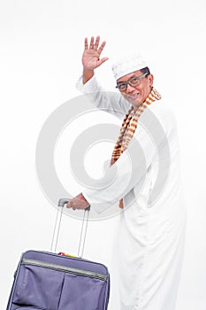 Portrait  old asian muslim man wear white clothes with travel suitcase from behind. waving and going for ramadan eid mubarak