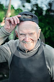 Portrait of an old farmer in a baseball cap. The 87 - year-old smiles and adjusts his baseball cap after work. Active ageing. To