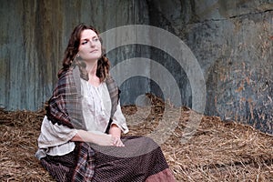 Portrait of an old-fashioned young woman sitting on a hay
