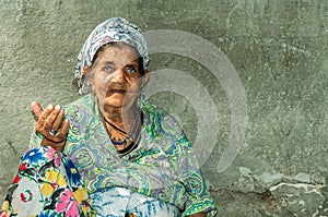 Portrait of old homeless Gypsy beggar woman with wrinkled face skin begging for money on the street in the city and looki