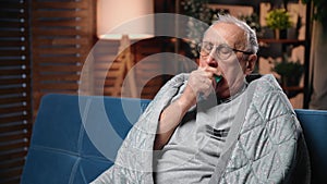 Portrait of old man with COVID or influenza virus in home, person coughing and wrapping in blanket