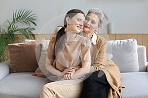 Portrait of old mother and mature daughter hugging at home. Happy senior mom and adult daughter embracing on sofa