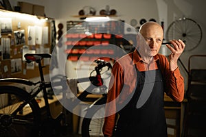 Portrait of old repair man in bicycle shop listening audio message working in cycling workshop and startup. Elderly bike