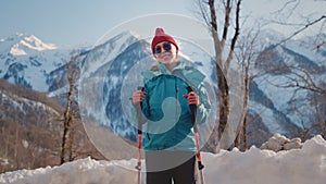 Portrait: old woman hiking in the winter mountains. Senior female uses sticks for Nordic walking