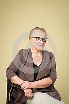 Portrait of an old woman wearing glasses on a wicker chair