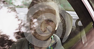 Portrait of an old woman with wrinkles through an car window.