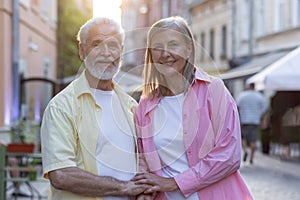 Portrait of an older couple, a man and a woman standing together on a city street, hugging and holding hands, smiling