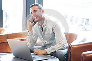 Older guy with laptop talking on mobile phone at cafe