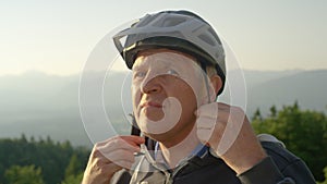 PORTRAIT: Older man puts on a helmet before a bicycle ride on a sunny evening.