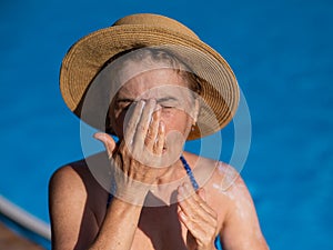Portrait of an older woman applying sunscreen to her face while on vacation.