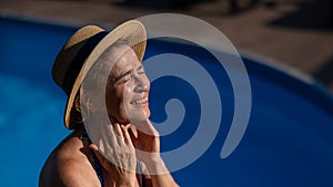 Portrait of an older woman applying sunscreen to her face while on vacation.