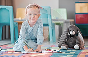 Portrait of one adorable little caucasian girl with a stuffed rabbit kneeling on the floor and drawing. Smiling orphan