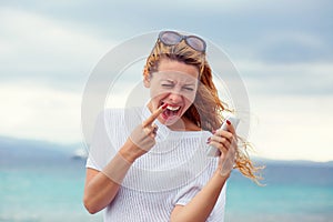 Portrait one angry young woman screaming on mobile phone standing outside with sea  background. Negative emotions feelings