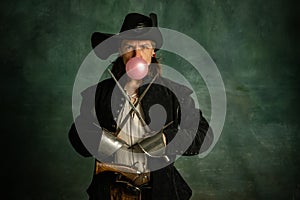 Portrait of one brutal man, medeival pirate crossing swords and inflating gum isolated over dark background.