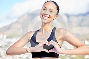 Portrait of one confident young mixed race woman gesturing a heart shape with her hands while exercising outdoors. Happy