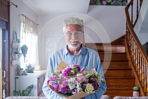 Portrait of one happy and cute old man holding flowers to give to his wife or girlfriends. Senior looking at the camera at home