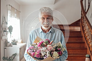 Portrait of one happy and cute old man holding flowers to give to his wife or girlfriends. Senior looking at the camera at home
