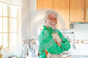 Portrait of one mature man or senior smiling and looking at the camera cooking in the kitchen at home