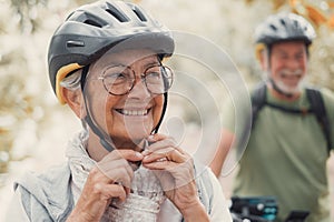 Portrait of one old woman smiling and enjoying nature outdoors riding bike with her husband laughing. Headshot of mature female