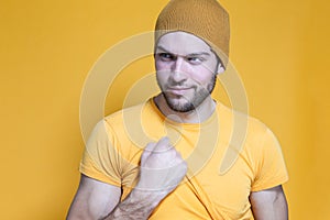 Portrait of One Positive Caucasian Handsome Man In Yellow Tshirt Posing in Warm Hat Over Yellow Background While Pulling Shirt Off