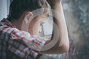 Portrait one sad little boy sitting near a window