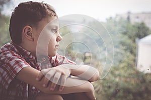 Portrait one sad little boy sitting near a window