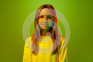 Portrait of one smiling pretty little girl, pupil dressed casually against green studio background in mixed neon light
