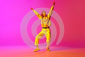 Portrait with one young girl, dancer with dreadlocks dancing with hands up over gradient pink background in neon light