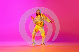 Portrait with one young girl, dancer with dreadlocks dancing over gradient pink background in neon light. Contemporary