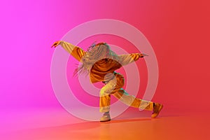 Portrait with one young girl, dancer with pigtails dancing with passion over gradient pink background in neon light