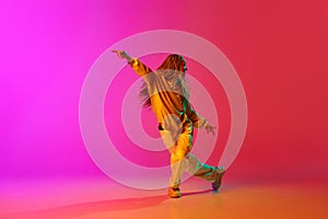 Portrait with one young girl, inspired dancer with pigtails dancing with passion over gradient pink background in neon