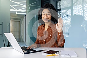 Portrait of online customer service call center worker, woman smiling and looking at camera, waving hand gesture of