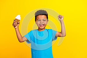 Portrait of optimistic little schoolboy with afro hair wear blue t-shirt hold ice cream clenching fist  on vivid