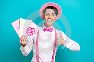 Portrait of optimistic man dressed pink retro cap bow tie white shirt hold postcards show thumb up isolated on blue
