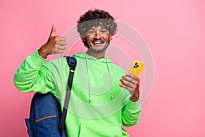 Portrait of optimistic new iphone user young arabian curly haired guy shows like symbol thumb up isolated on pink color