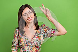 Portrait of optimistic nice young woman brown hair stylish shirt showing v-sign greetings symbol hello isolated on green