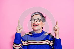 Portrait of optimistic pleasant woman wear striped pullover directing look up at offer empty space isolated on pink