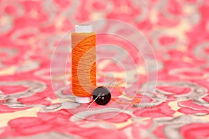 Portrait of orange sewing thread, needle and button