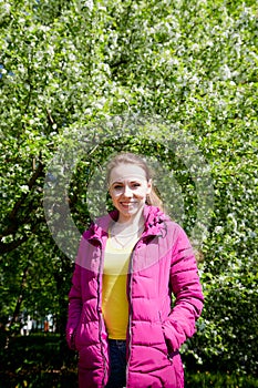 Portrait of a ordinary cute girl in the green park full of blossoming apple tree with white flower in a springtime