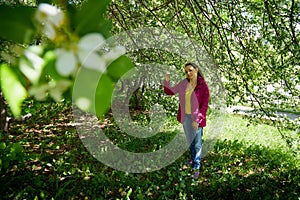 Portrait of a ordinary cute girl in the green park full of blossoming apple tree with white flower in a springtime