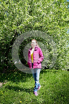 Portrait of a ordinary cute girl in the green park full of blossoming apple tree with white flower in a springtime