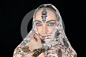 Portrait of an oriental young woman in a scarf with an ornament and jewels on a black background