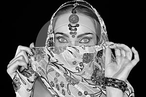 Portrait of an oriental young woman in a scarf with an ornament and jewels in black and white