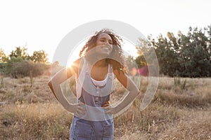 Portrait outdoors of a beautiful happy young afro american woman smiling at sunset. Yellow background. Lifestyle in nature. Casual