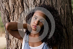 Portrait outdoors of a beautiful young afro american woman smiling at sunset. Brown tree background. Lifestyle in nature. Casual