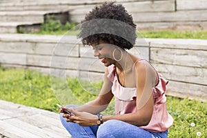 portrait outdoors of a beautiful young afro american woman at sunset using mobile phone. wood background.