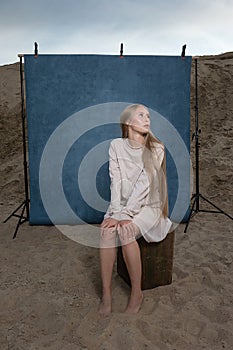 Portrait outdoors on sand in front of blue studio backdrop, pretty female posing