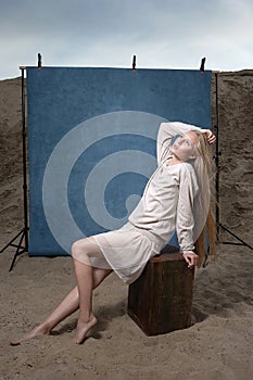 Portrait outdoors on sand in front of blue studio backdrop, pretty female posing