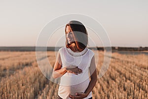 Portrait outdoors of a young beautiful pregnant woman touching her belly while expecting a baby. Outdoors lifestyle. Yellow